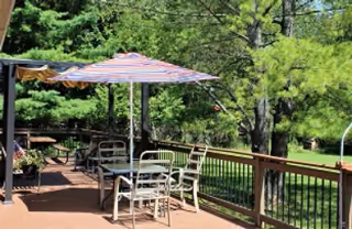Wooden outdoor deck with a patio table, chairs and umbrella overlooking a grassy yard and trees.