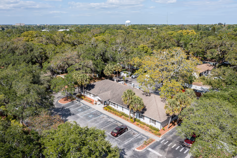 Aerial view of a single-story senior living building surrounded by trees with a parking lot and a few cars.