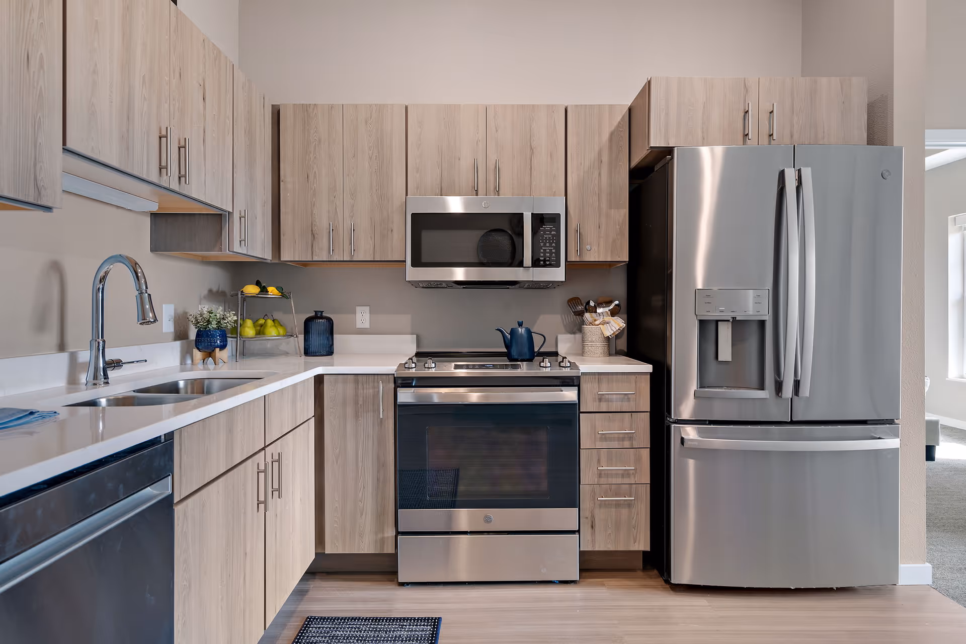 A modern kitchen with light wood cabinets, quartz countertops, and stainless steel appliances including a French-door refrigerator, stove, and microwave.