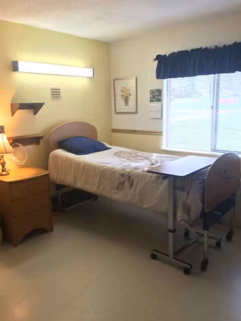 A compact bedroom with a single bed, nightstand, desk, and window with curtains.