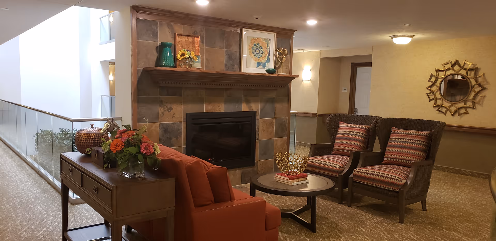 Cozy indoor seating area with an upholstered sofa, two patterned armchairs, round coffee table, decorative fireplace and console table with flowers.