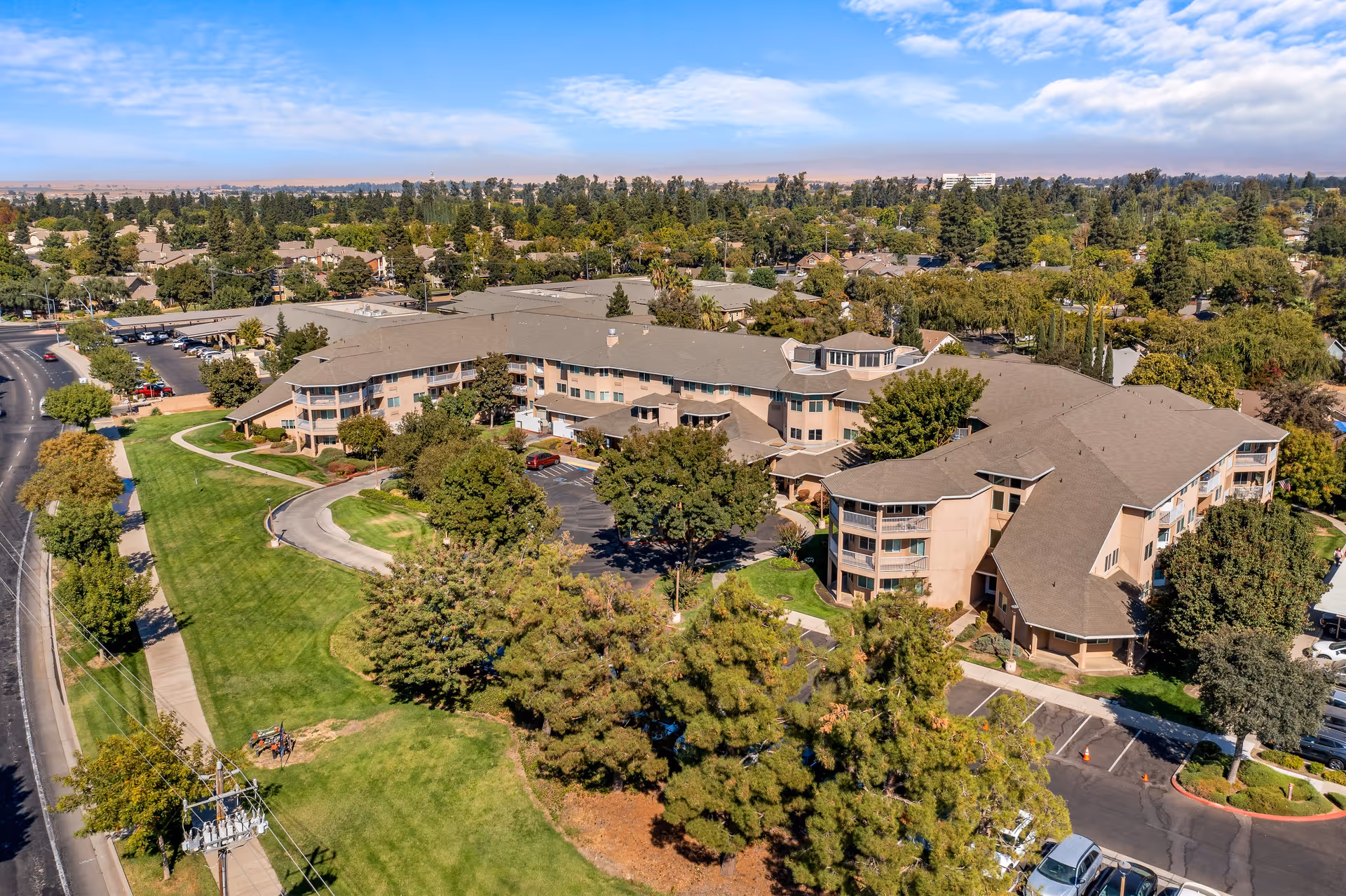 Aerial view of The Hampshire - A Provincial Senior Living Community, showing a large multi-wing building surrounded by green lawns, trees, and parking areas under a partly cloudy sky.