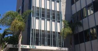 Tall glass-front building with palm trees, sign reading Country Villa Rehabilitation Center at entrance.