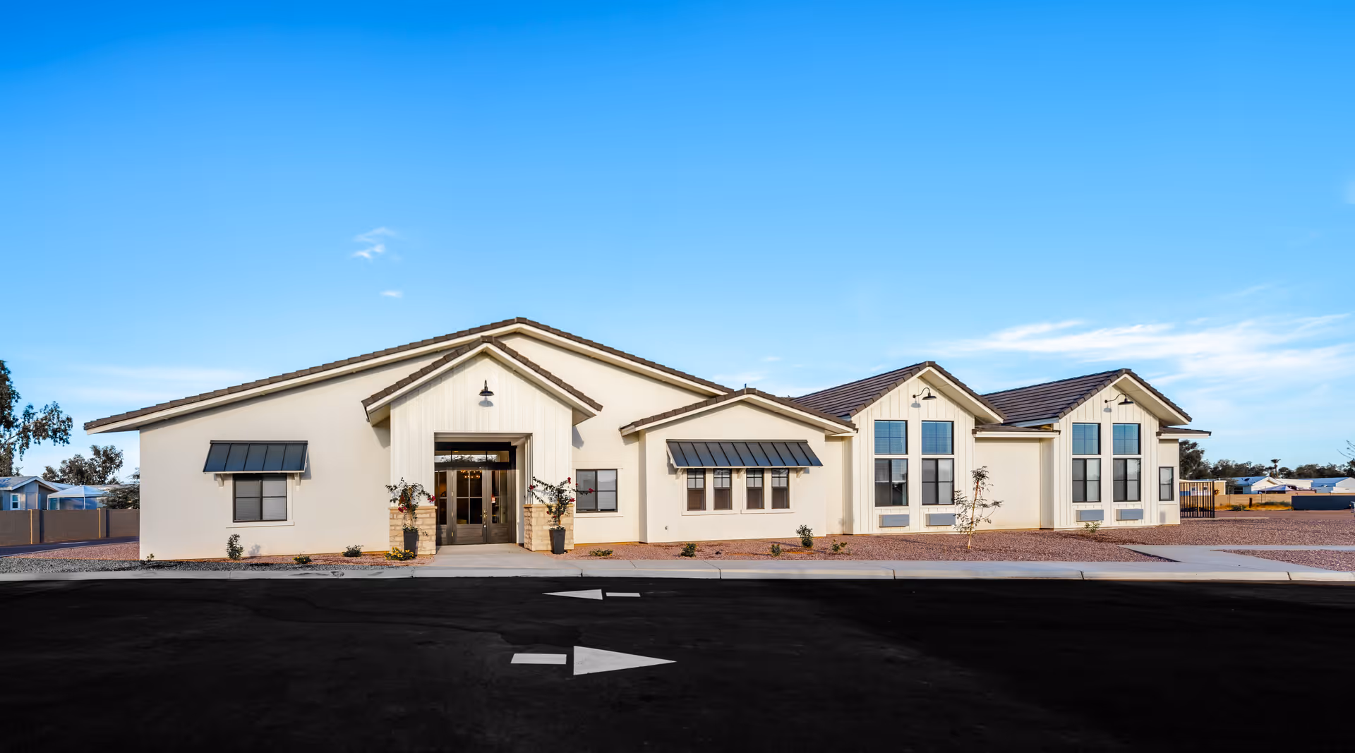 Single-story light-colored assisted living building with multiple gabled roofs, central entrance, and a paved driveway under a clear blue sky.