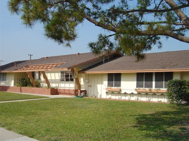 Single-story beige building with a brown roof, front lawn, and tree branches in the foreground.