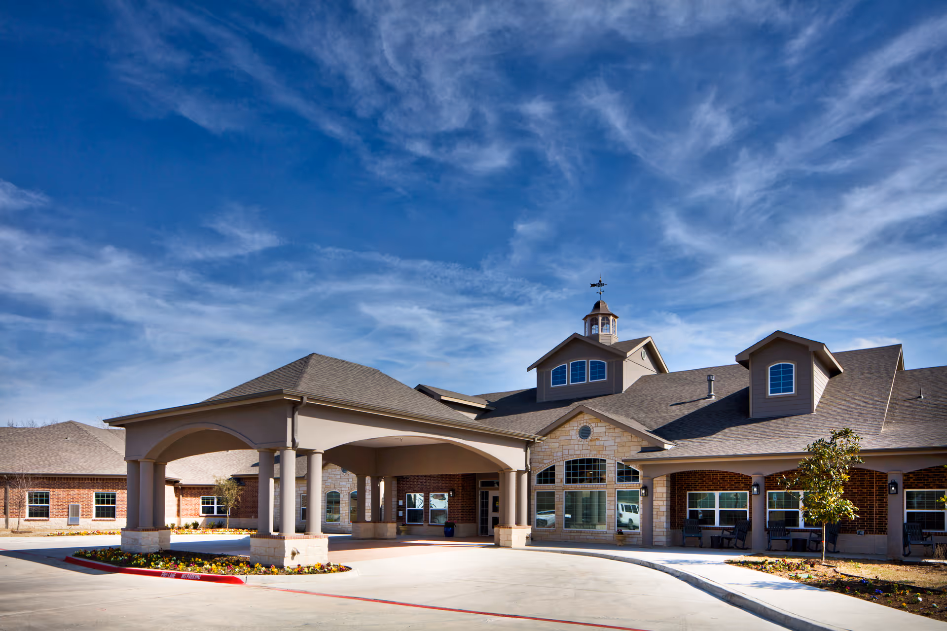 Front entrance and porte-cochere of a senior living facility building under a blue sky.
