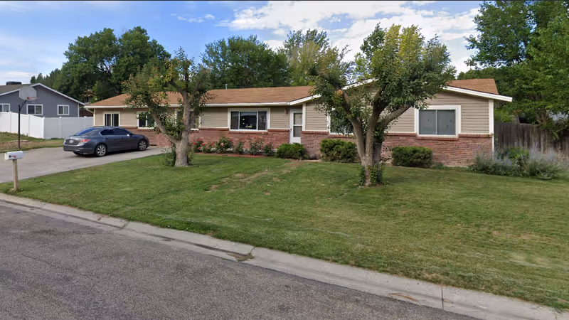 Single-story facility exterior with lawn, trees, driveway, and a parked car in front.