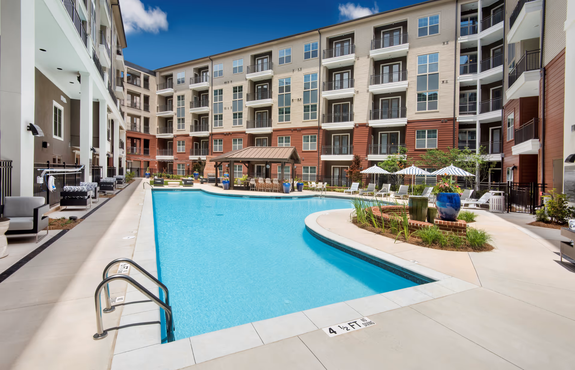 Courtyard swimming pool with lounge chairs, umbrellas, planters, and a multi-story residential building surrounding it.