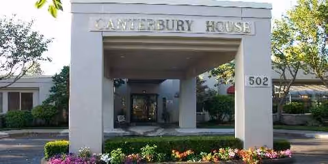 Front entrance of Canterbury House senior living facility with a covered walkway and landscaped surroundings.