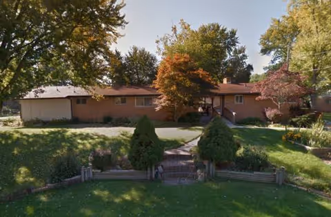Single-story brick senior living facility with front lawn, stairs, and trees.