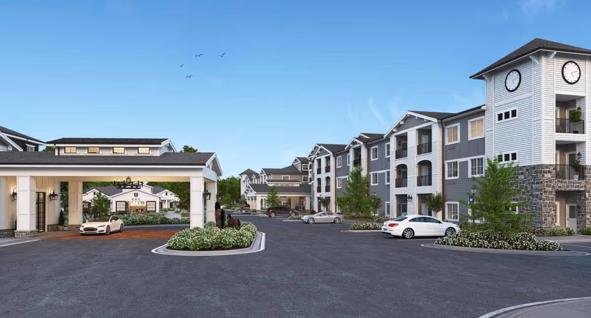 Exterior view of The Park at University Village Independent Living Community showing multiple connected buildings with gray and white siding, a clock tower, landscaped areas with bushes and trees, parked cars, and a covered entrance under a clear blue sky with birds flying.