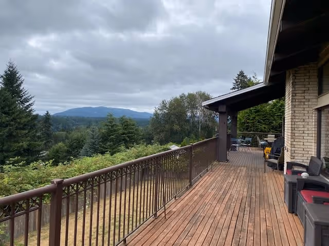 Wooden deck with railing overlooking trees and distant forested hills under a cloudy sky.