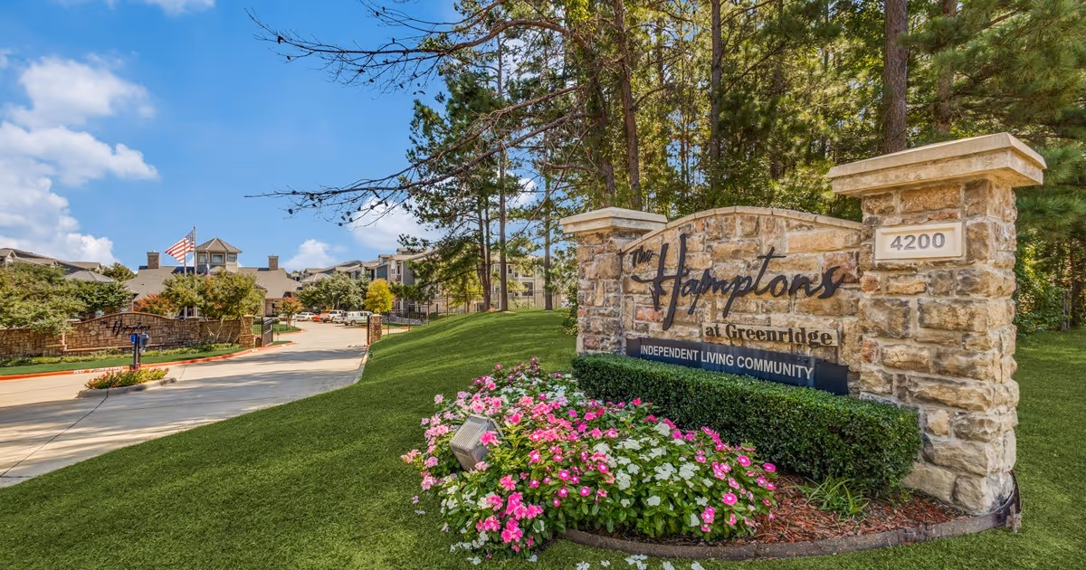 Stone entrance sign reading 'The Hamptons at Greenridge Independent Living Community' beside a driveway and landscaped grounds.