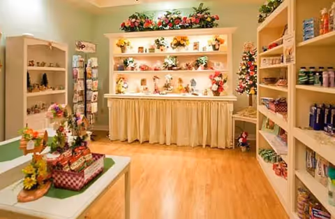 A bright interior gift shop area with shelves and tables displaying flowers, decorative items, and personal care products.