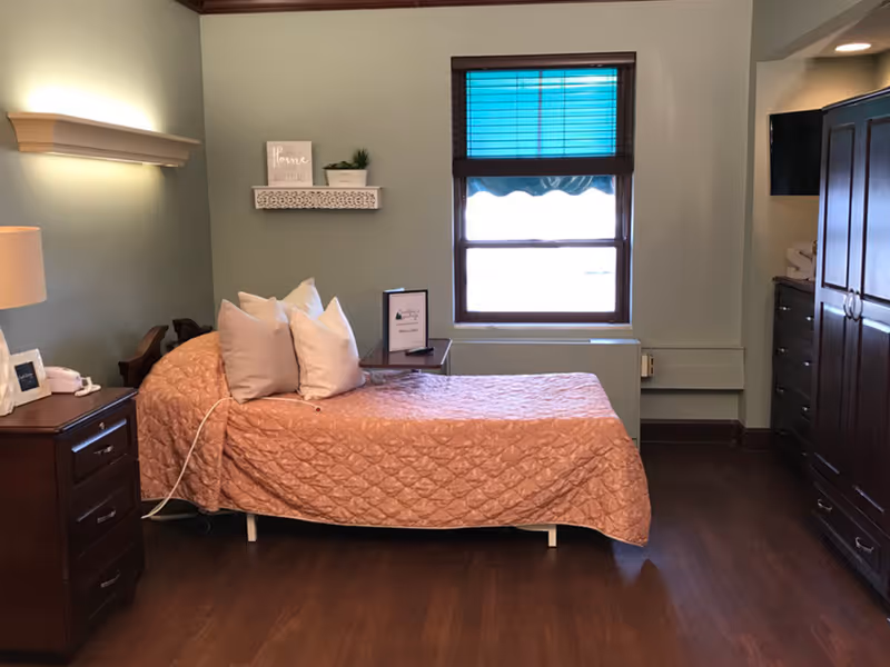 Single-occupancy bedroom with a made bed, pillows, wooden nightstands and wardrobe, and a window.