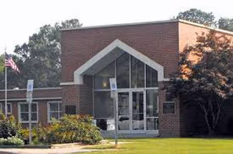 Brick senior living facility entrance with glass doors and landscaping.