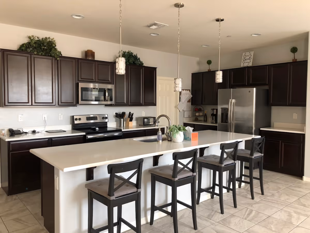 Spacious modern kitchen featuring a long white island with four bar stools, dark wood cabinets, and stainless steel appliances.
