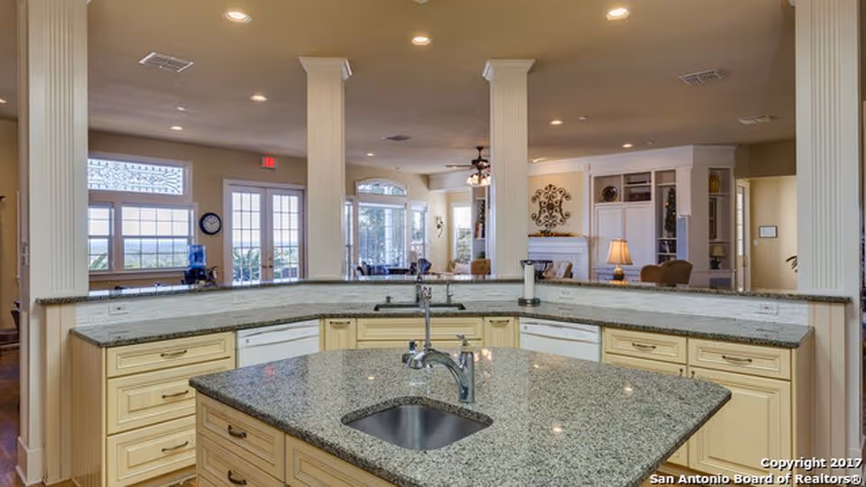 Open kitchen featuring a large granite island with a sink and cabinetry overlooking a bright open living area.