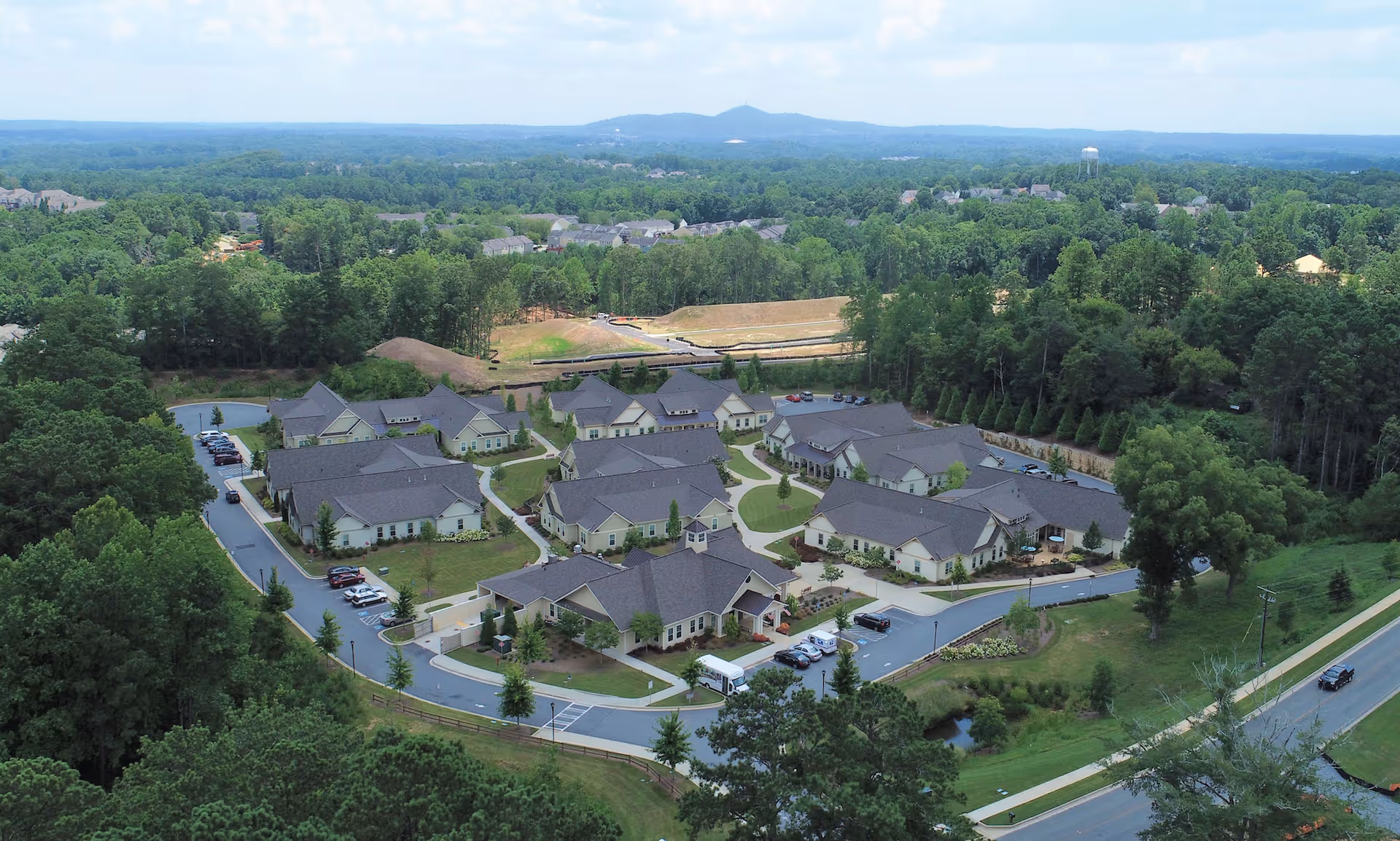 Aerial view of a senior living community with multiple single-story residential buildings, driveways, parking areas, and surrounding trees.