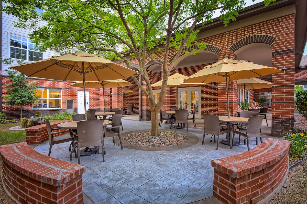 Courtyard with round tables and yellow umbrellas around a central tree in front of a red brick building.