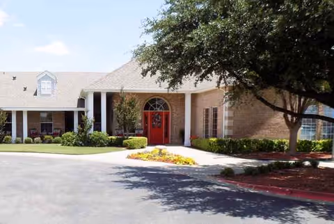 Front view of a brick senior living facility with a red door and landscaped grounds.