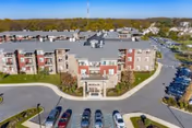 Aerial view of a three-story senior living building with a central entrance, curved driveway and parked cars in front.