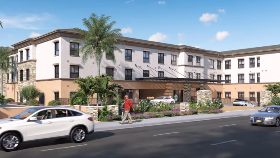 Modern senior living facility exterior with palm trees and a driveway entrance.