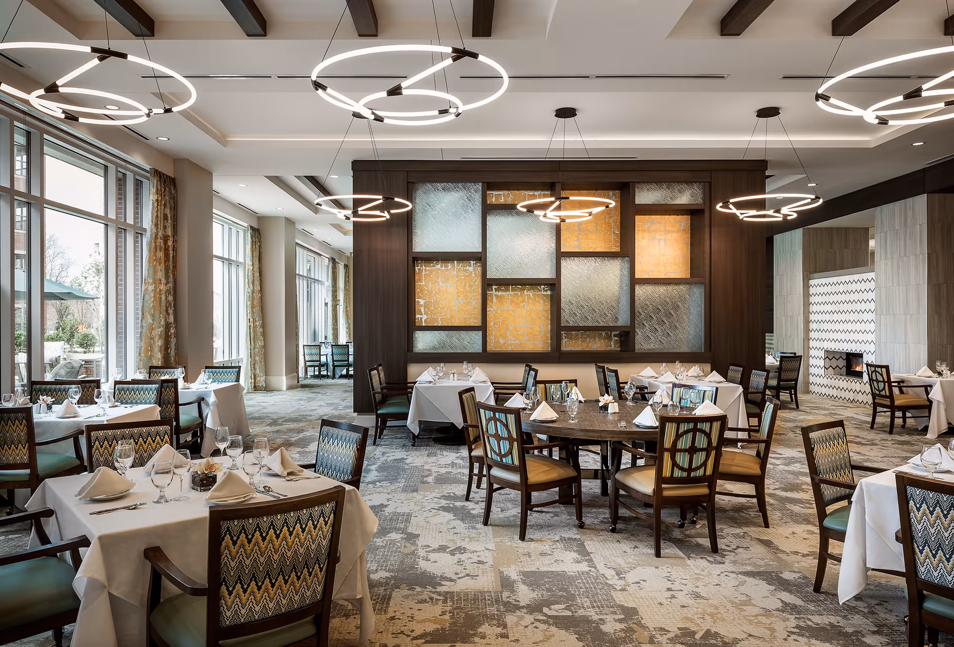 Elegant dining room with multiple set tables, modern circular chandeliers, and large windows.