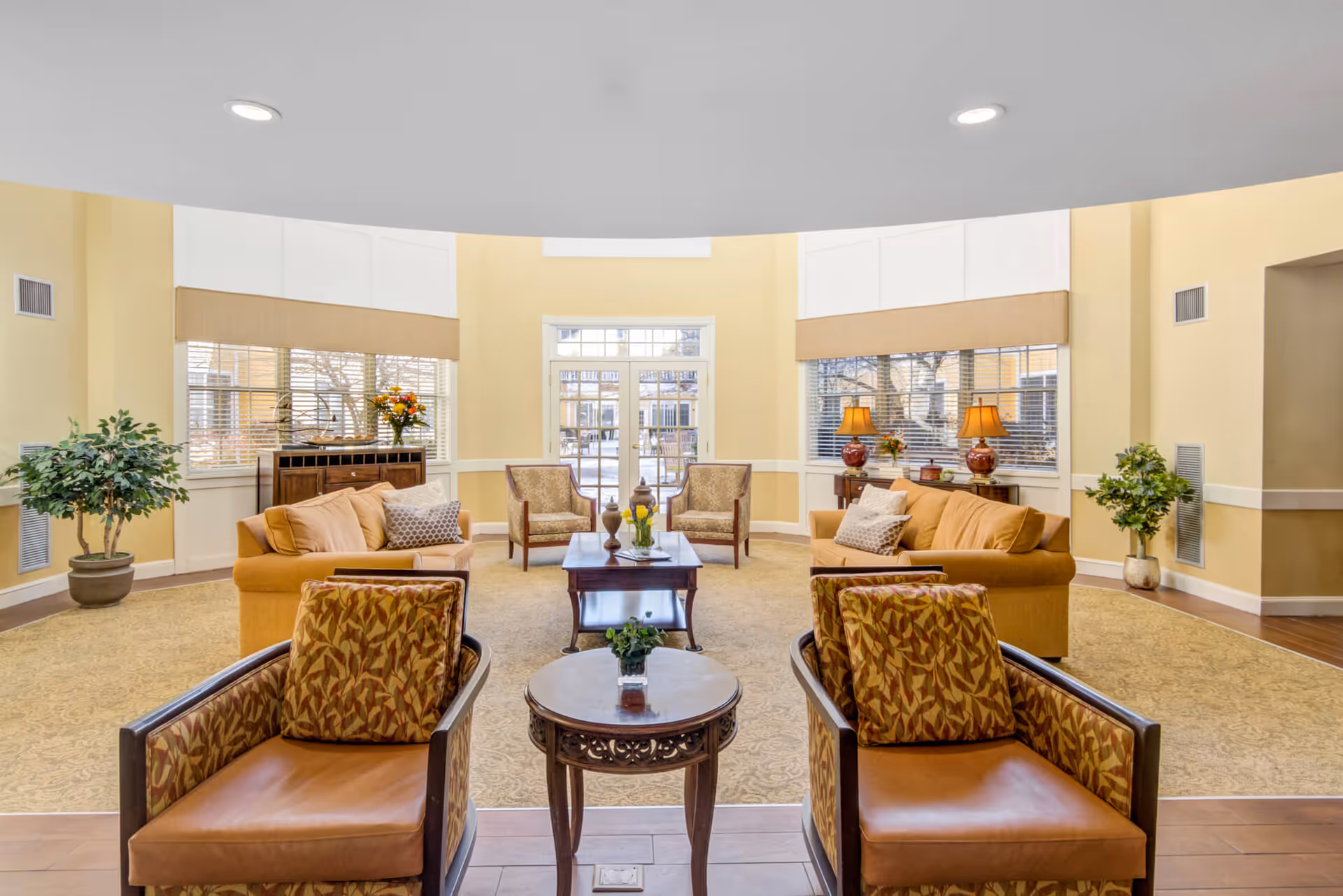 Bright, spacious senior living lounge with sofas, armchairs, coffee tables and large windows.