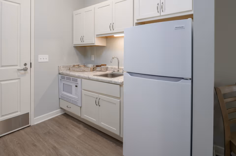 Small kitchenette with white cabinets, a sink, countertop, built-in microwave, and a white refrigerator.