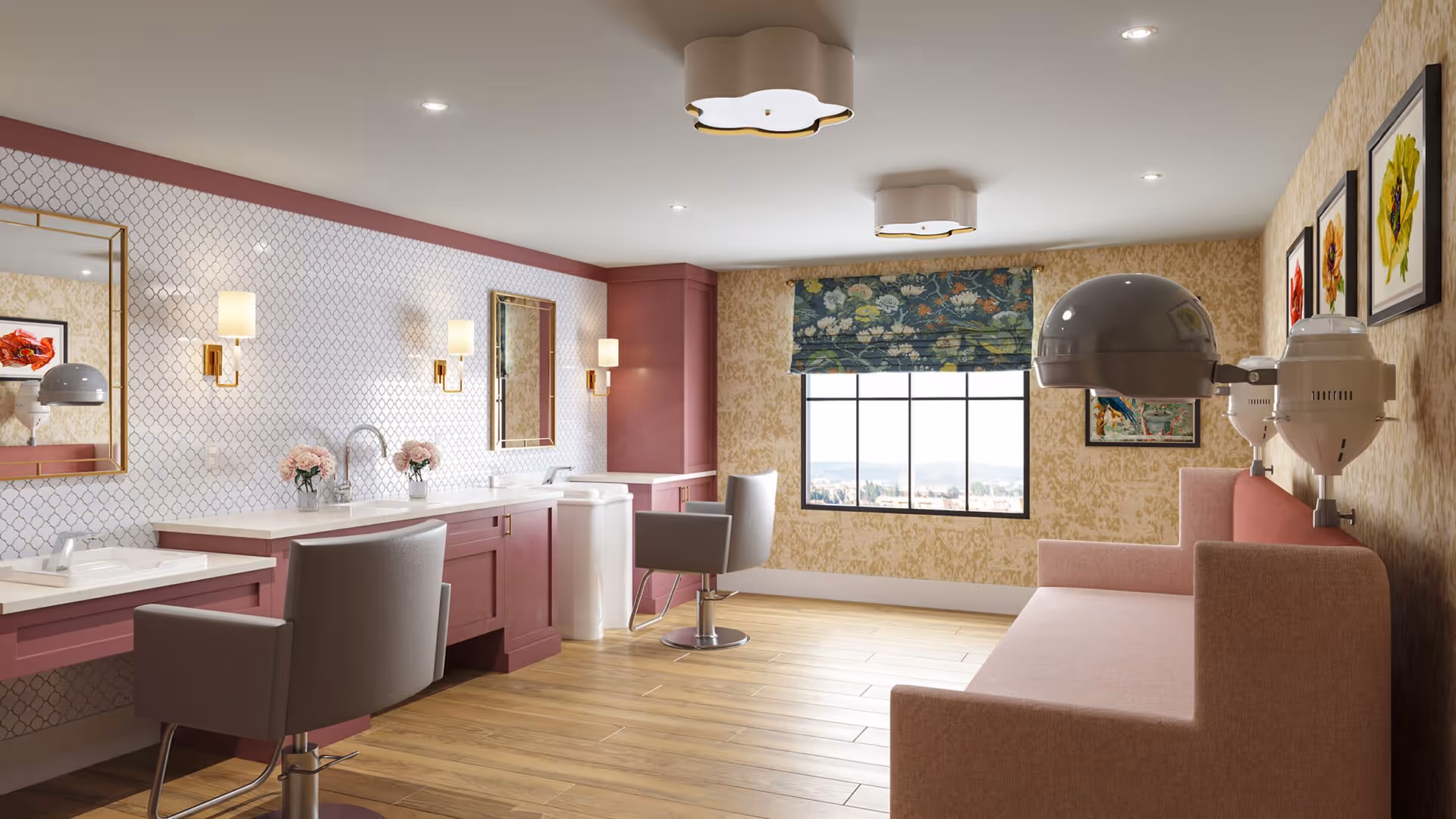A bright and stylish salon room with two salon chairs in front of a long counter with sinks and mirrors. The walls have patterned wallpaper, and there are two hair dryers mounted above a pink cushioned bench. A window with a floral Roman shade lets in natural light, and framed floral artwork decorates the walls.