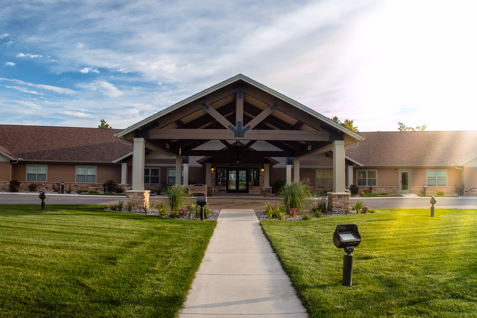 Front exterior view of Teal Lake Senior Living Community building with a covered entrance, well-maintained green lawn, and a partly cloudy sky.