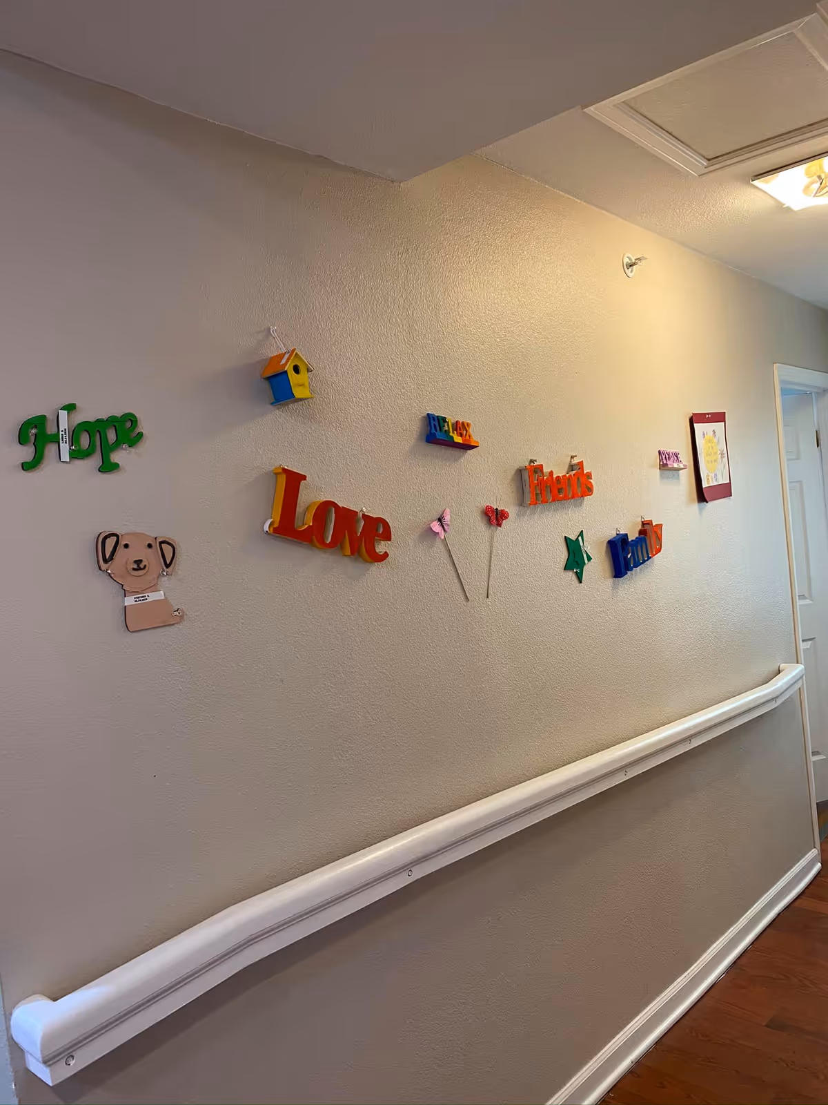 A well-lit interior hallway wall with a white handrail and colorful decorative words and shapes like 'Love', 'Hope', and 'Friends' mounted on the wall.