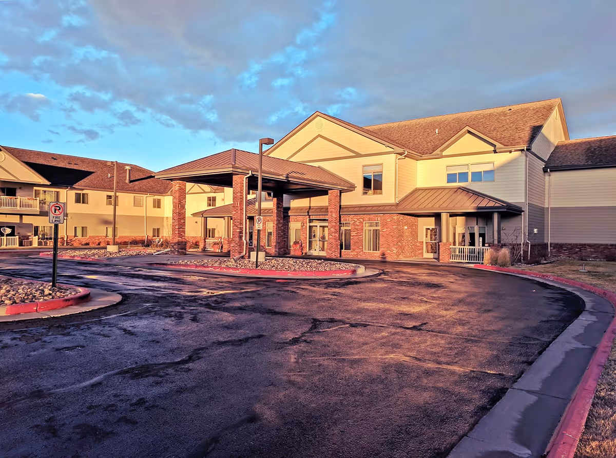 Exterior view of Primrose Retirement Community of Casper building during sunset with a covered entrance, paved driveway, and clear sky with some clouds.