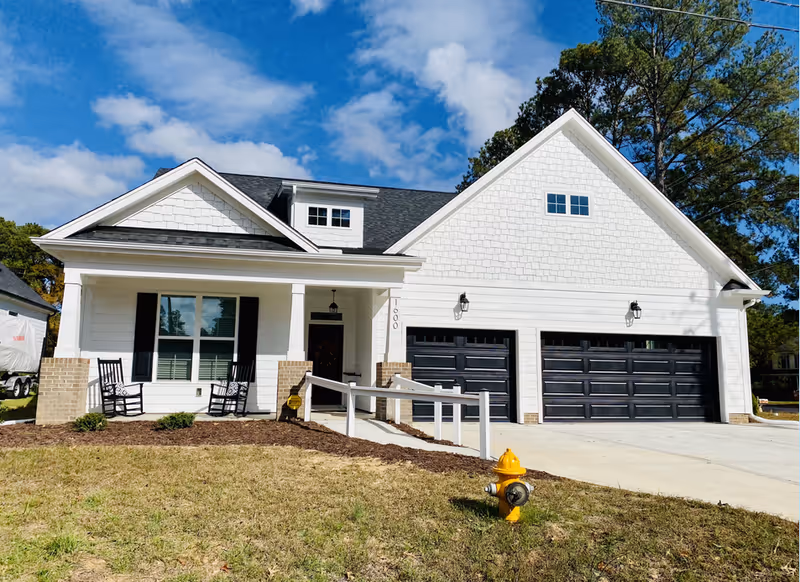 Front exterior of a white single-family house with a covered porch, wheelchair ramp, and attached three-car garage.