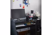 A small office desk against a white wall with a monitor, keyboard, mouse, PC tower, chair and assorted personal items and tissues.