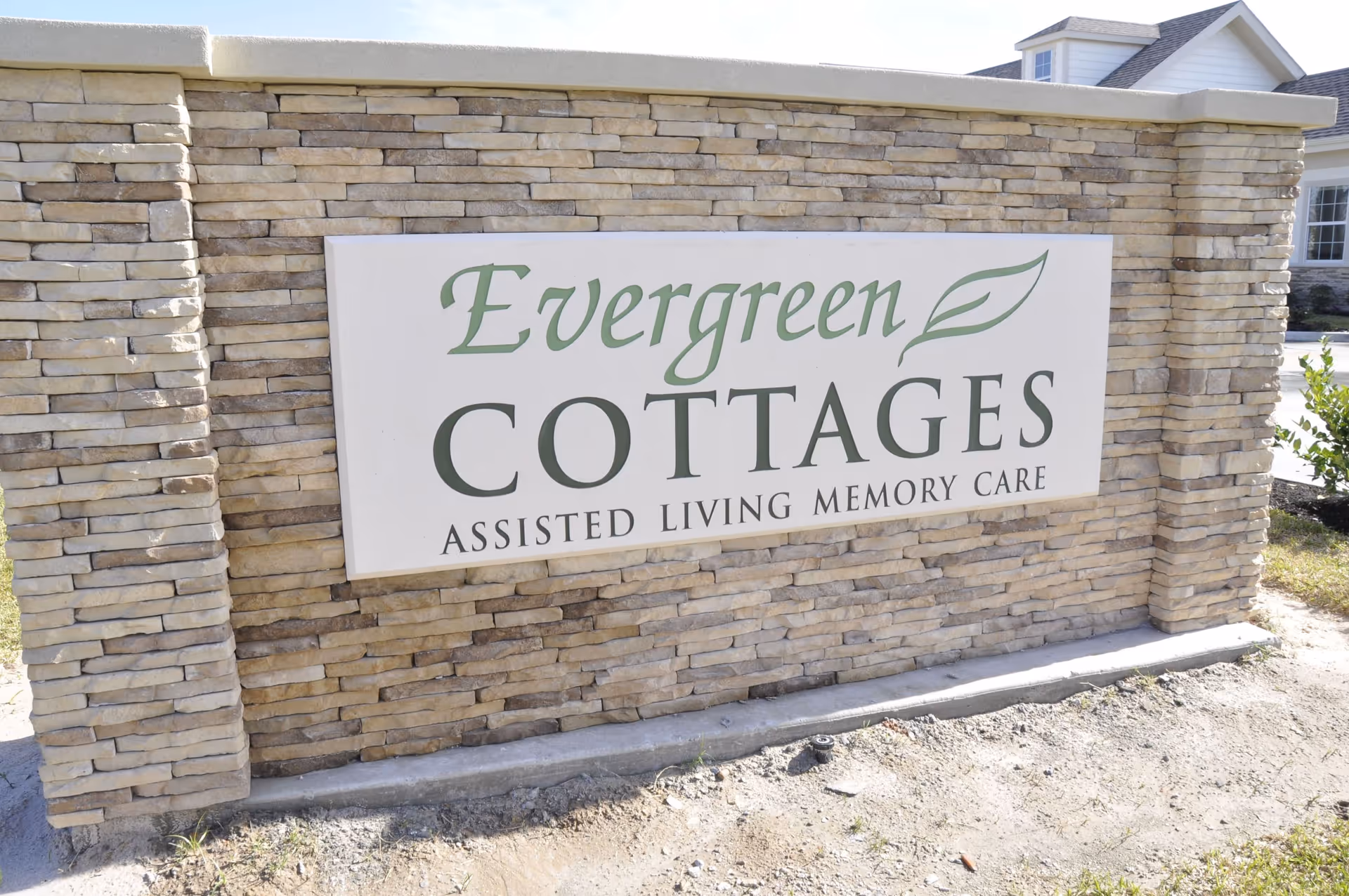 Stone entry sign reading "Evergreen Cottages Assisted Living Memory Care" in front of a building.