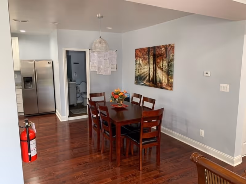 A dining room with a dark wooden table and chairs, wall art, and a fire extinguisher.