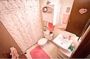 Small bathroom with a floral shower curtain, white toilet, white sink with a mirror above it, and pink bathroom accessories including a bath mat, towels, and a soap dispenser.