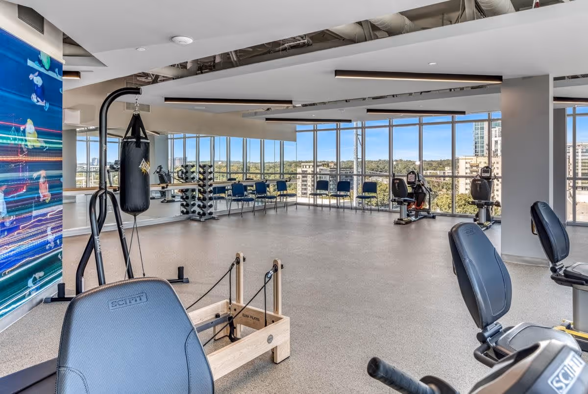 Bright senior living fitness center with exercise machines, a punching bag, free weights and floor-to-ceiling windows overlooking the city.