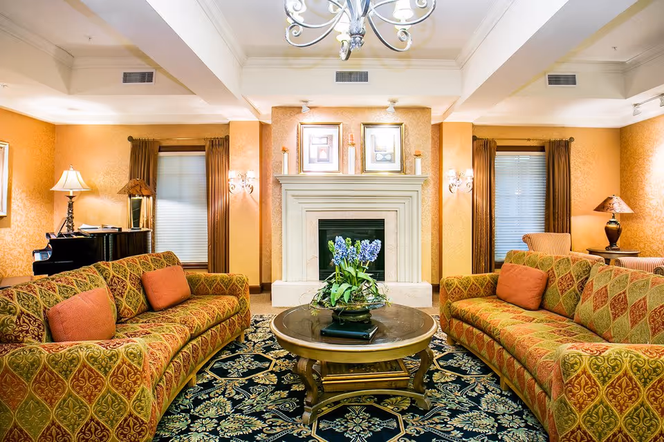 Warm, elegantly furnished living room with two patterned sofas around a round coffee table and a fireplace.