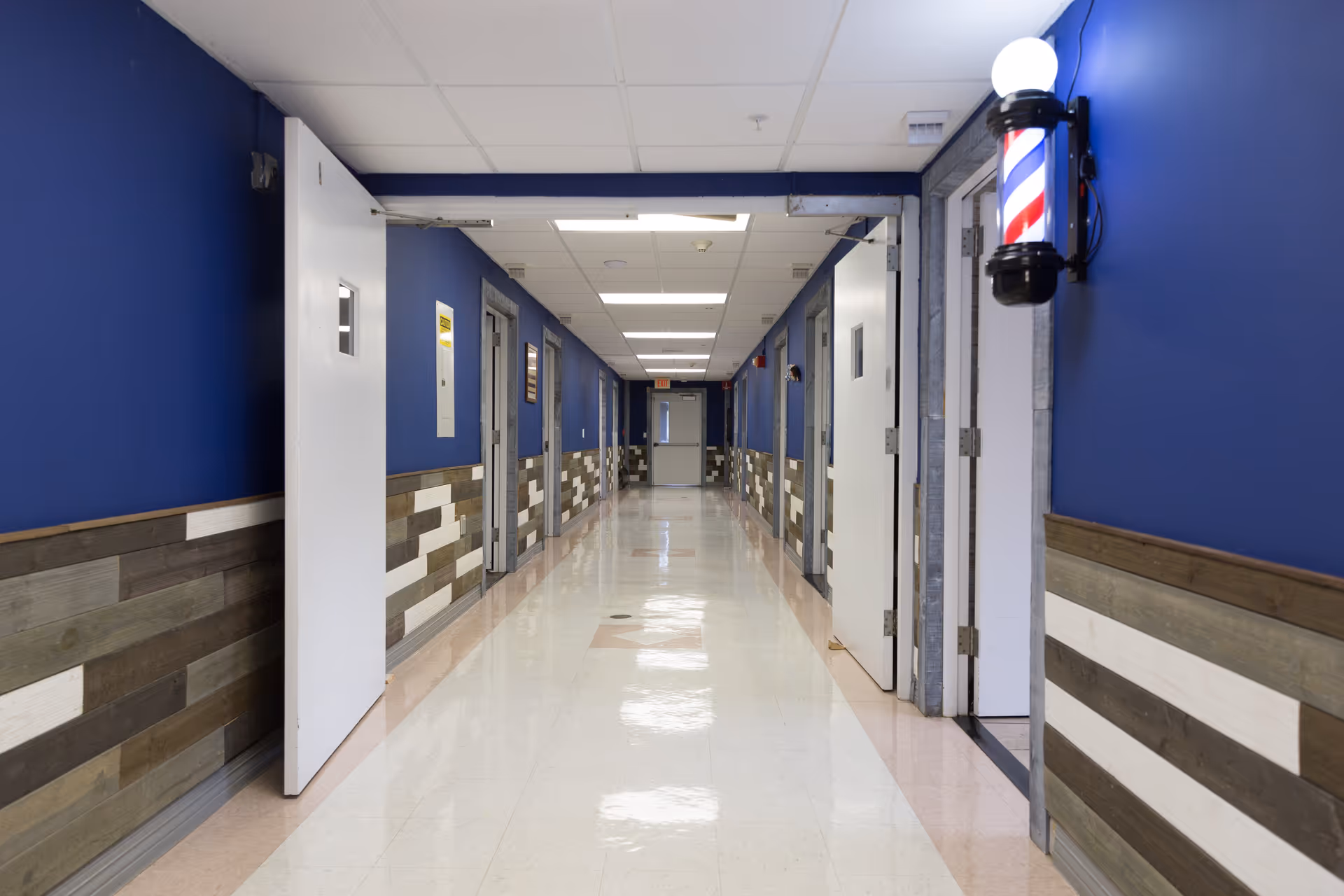 Long indoor hallway with blue walls, wood wainscoting, open doors and a barber pole light on the right.