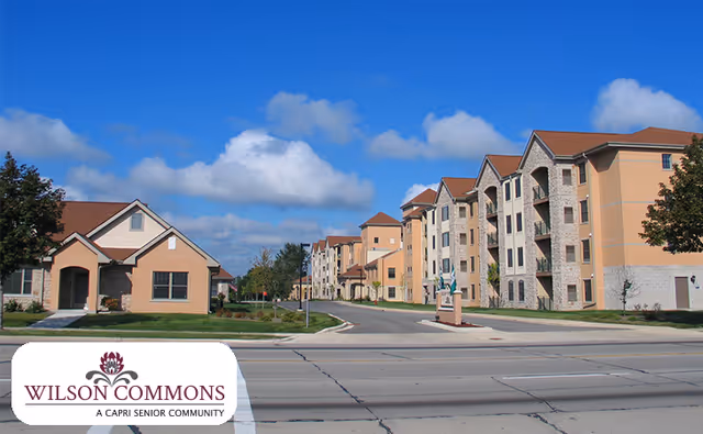 Exterior view of Wilson Commons senior living community showing multiple residential buildings along a street under a blue sky with some clouds.