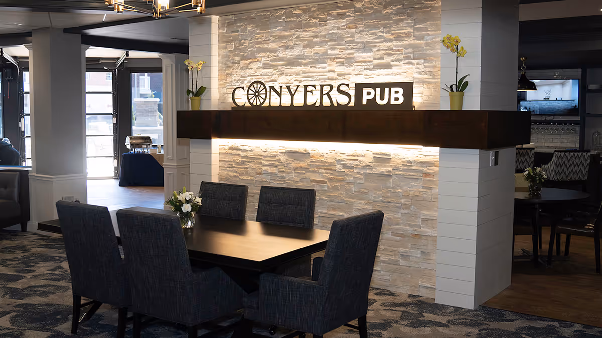 Interior dining area with a table and six chairs in front of a stone wall sign reading "Conyers Pub".