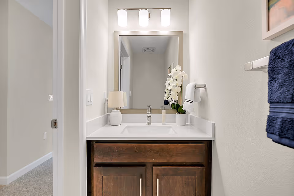 Small bathroom vanity with a white countertop, sink, mirror, light fixture, orchid and towels.