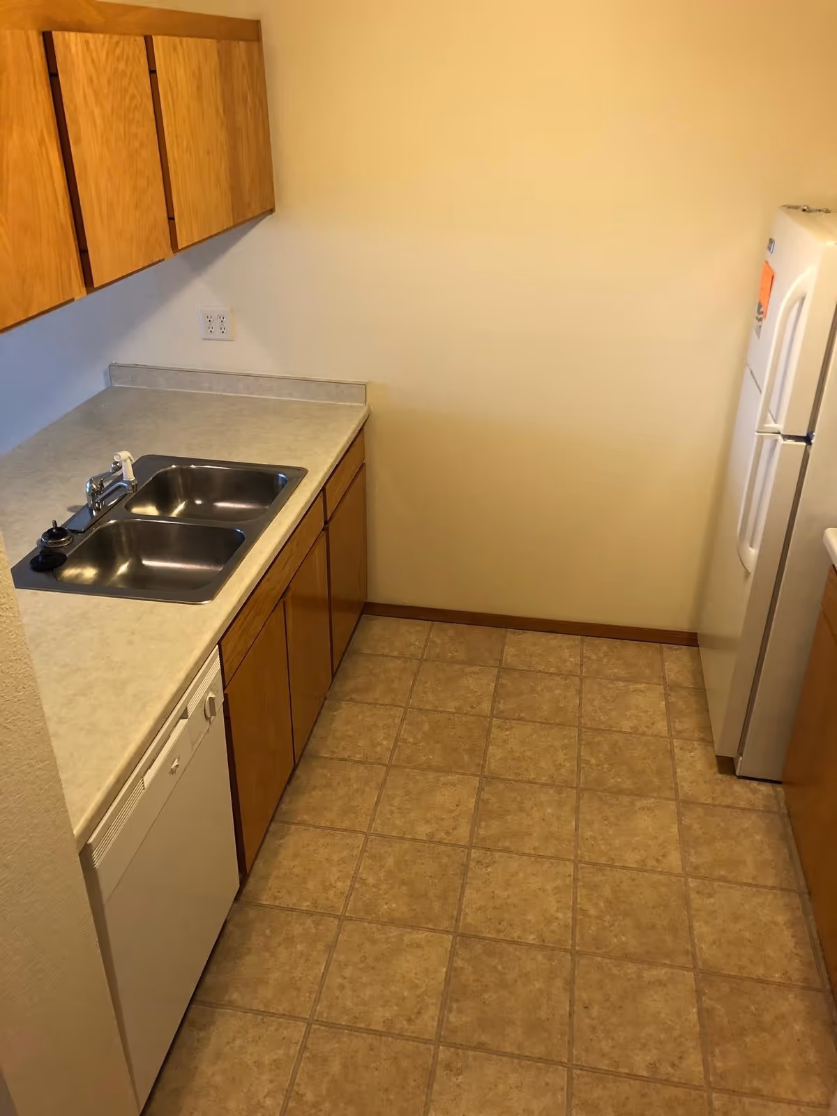 Small galley kitchen with a double stainless sink, laminate countertops, wooden cabinets, dishwasher and refrigerator.