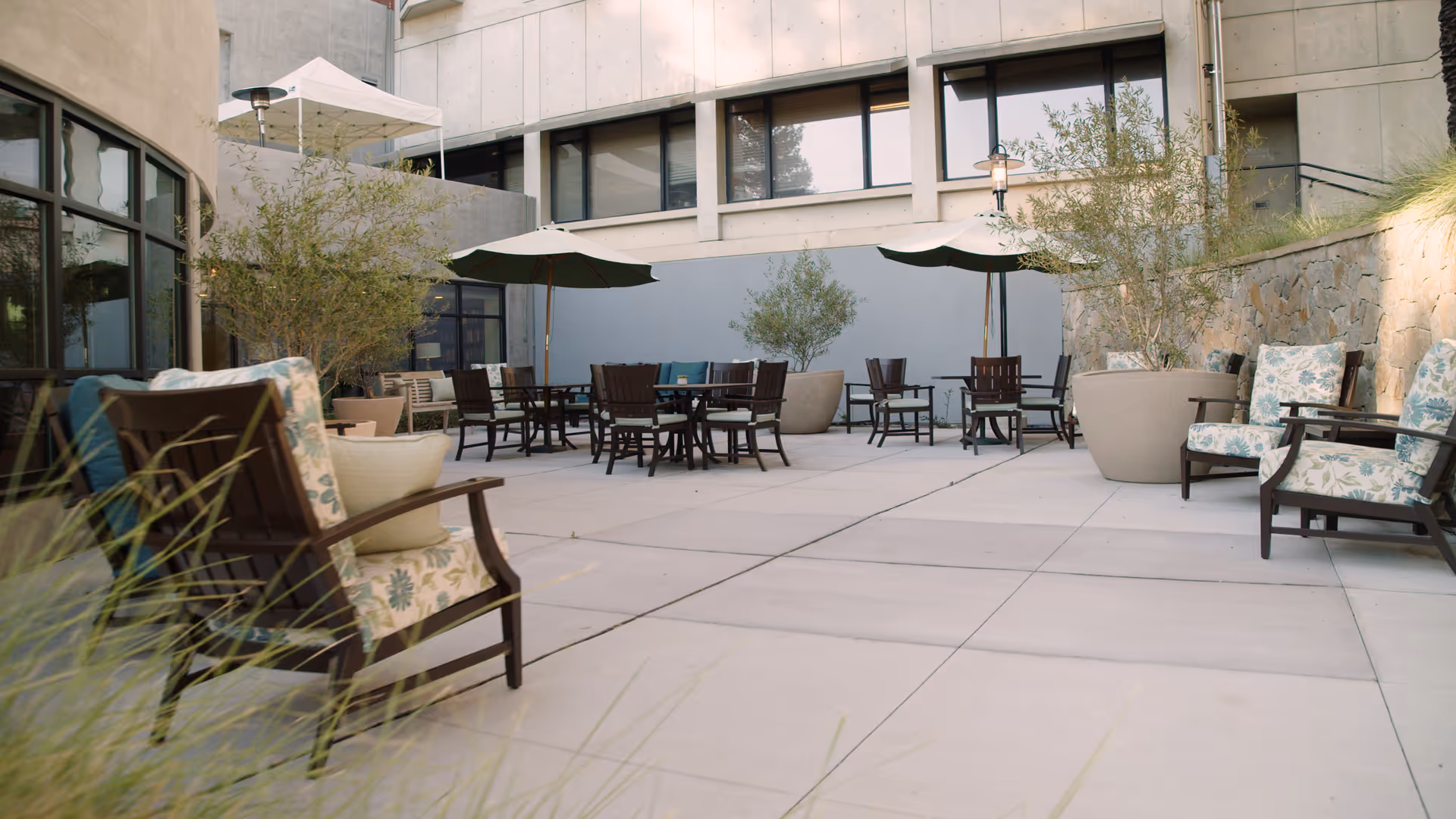 Outdoor courtyard patio with tables, umbrellas, potted plants and cushioned chairs at a retirement facility.