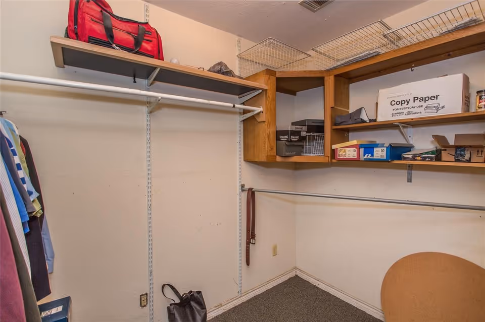Walk-in closet with wooden shelves, hanging rods, boxes, and a few clothes and bags.