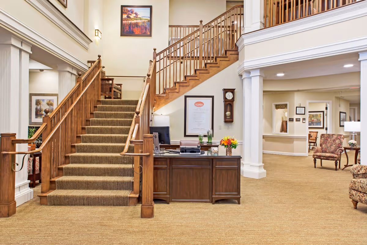 Carpeted lobby with a central wooden staircase, reception desk, and seating area.