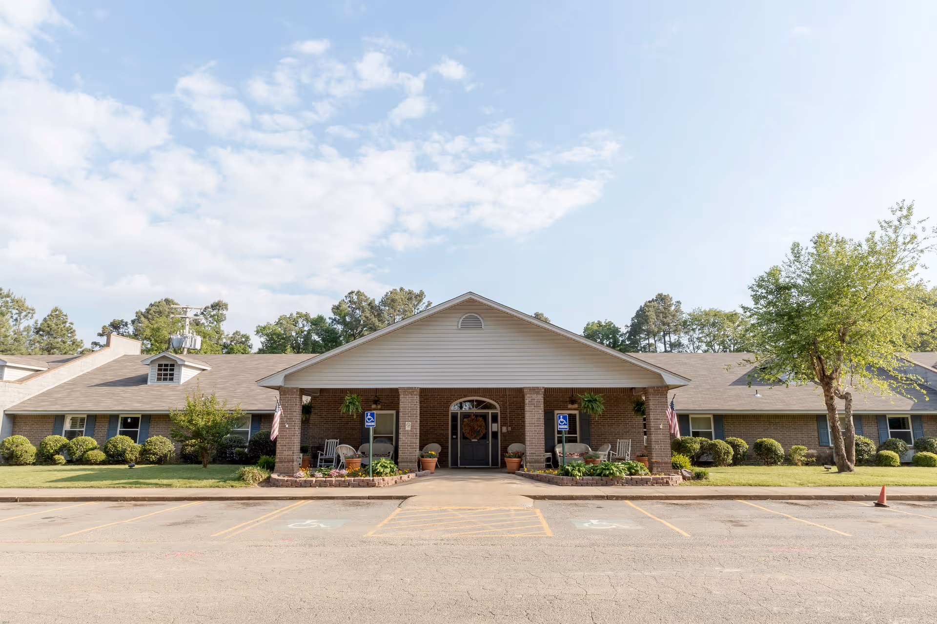 Front exterior view of Pleasant Valley Rehabilitation and Nursing facility showing a single-story brick building with a covered entrance supported by brick columns, surrounded by greenery and a parking area with handicap parking spaces.